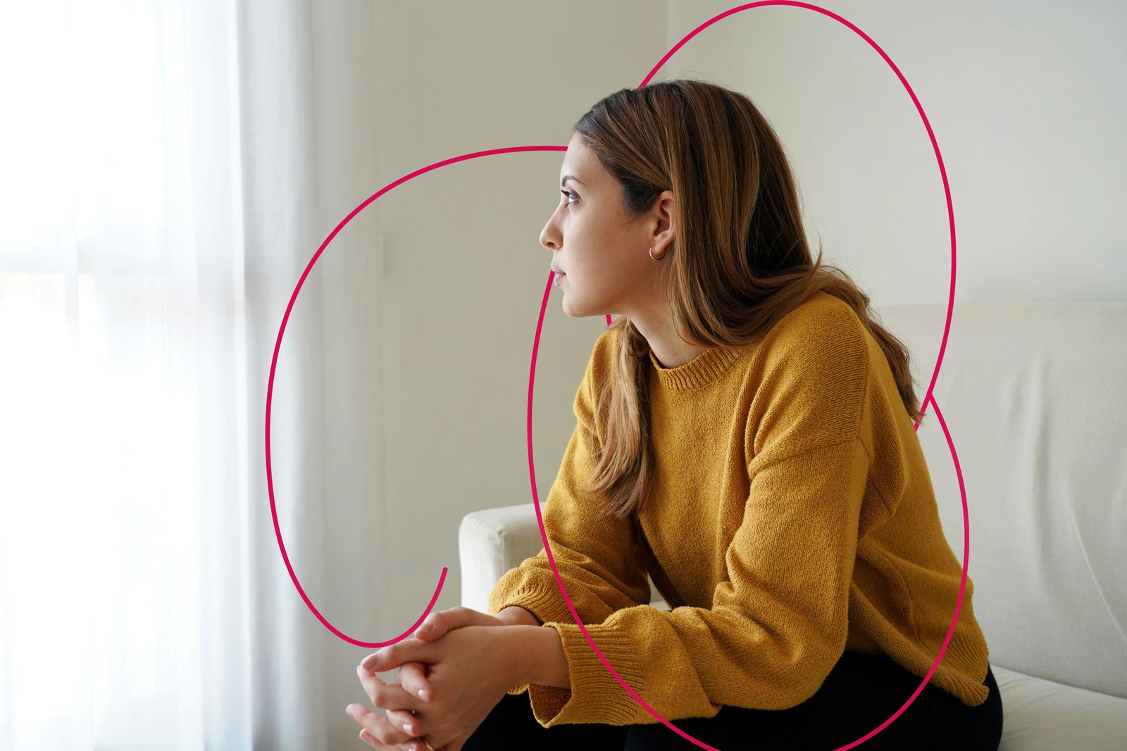 A young woman sitting on a sofa looking out of the window, thinking